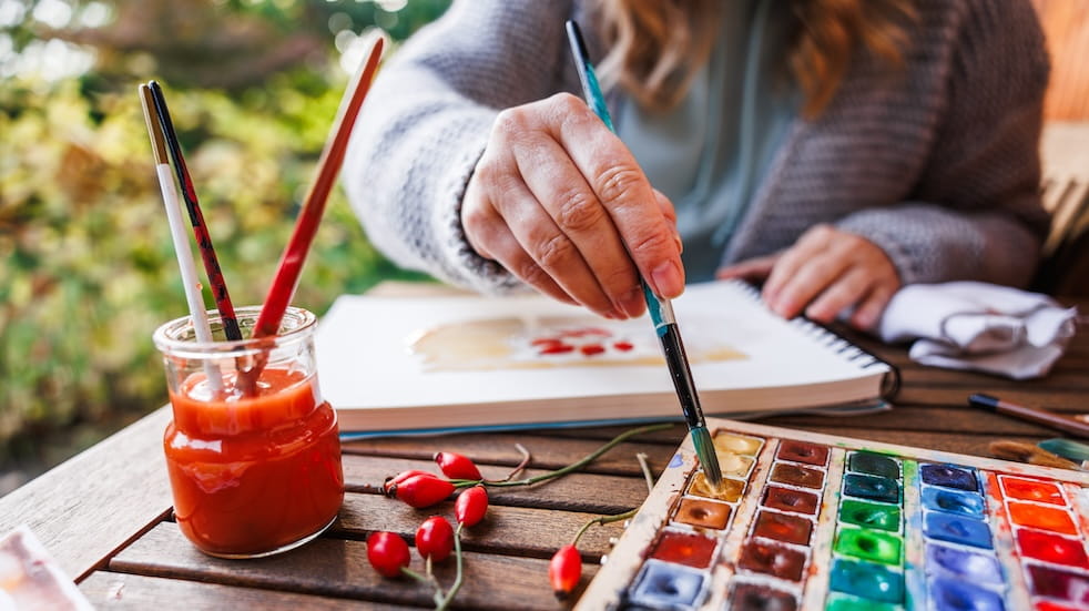 Woman artist dips paintbrush into water colour palette